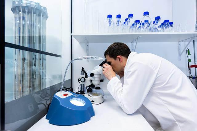 Lab assistant in a white lab coat looking in a microscope